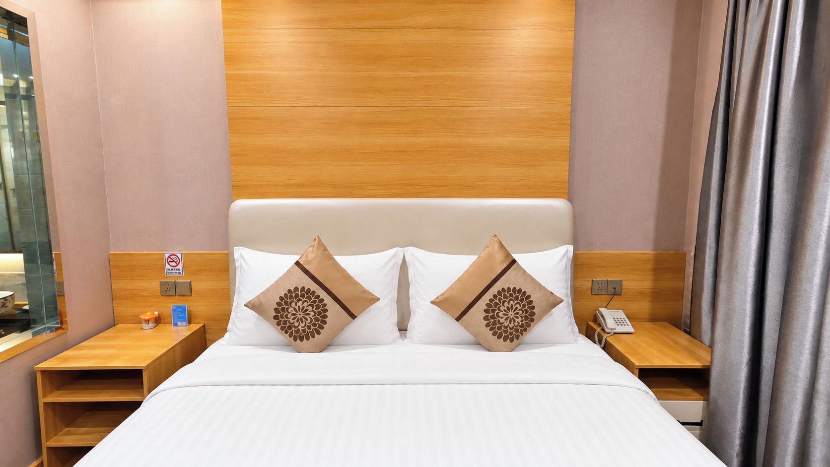 Une chambre d’hôtel avec une tête de lit en bois, deux tables de chevet, un lit avec une literie blanche et des coussins décoratifs.