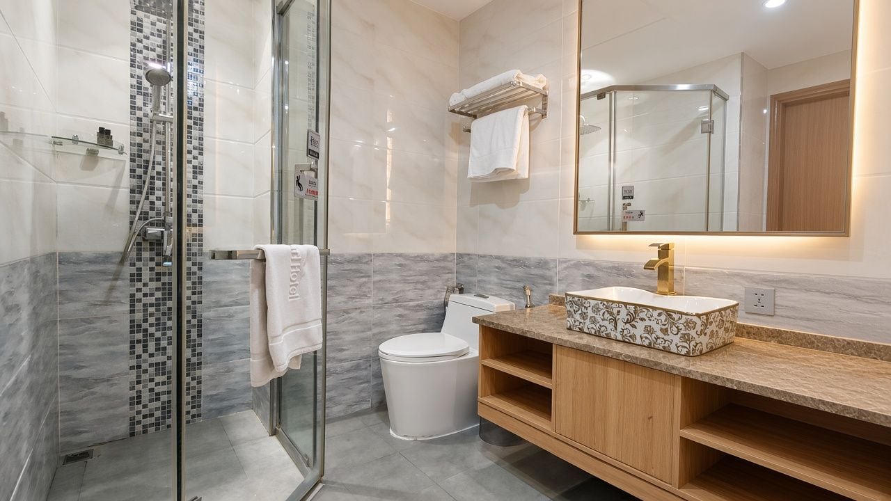 A modern bathroom with a glass shower enclosure, a toilet, a sink with a marble countertop, and a mirror with a wooden frame.