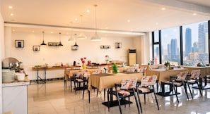 A modern dining area with multiple tables and chairs, a kitchen counter with dishes, and pendant lighting. - Diamond Pearl Hotel & Residence (Phnom Penh)