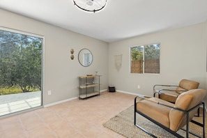 A spacious room with a large sliding glass door, a round mirror, a metal-framed sofa, and a small wooden side table.