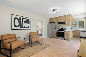 A modern kitchen with a refrigerator, microwave, and stove. There are two chairs and a rug in the living area.