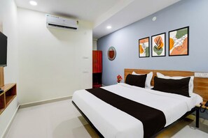 A hotel room with a bed, a TV, an air conditioner, a wooden headboard, and three framed artworks on the wall. - Townhouse Oak Kukatpally North (Hyderabad)