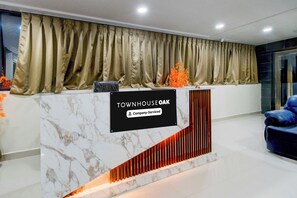 A reception desk with a marble top, a sign reading 'TOWNHOUSE OAK & Company Serviced', and a blue chair to the right. - Townhouse Oak Kukatpally North (Hyderabad)