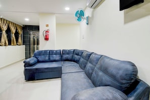 A room with a sectional sofa, a fire extinguisher, an air conditioning unit, and a ceiling fan. - Townhouse Oak Kukatpally North (Hyderabad)
