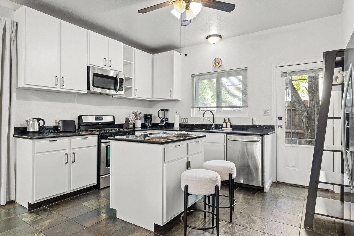 A modern kitchen with white cabinetry, a central island, stainless steel appliances, and a ceiling fan.