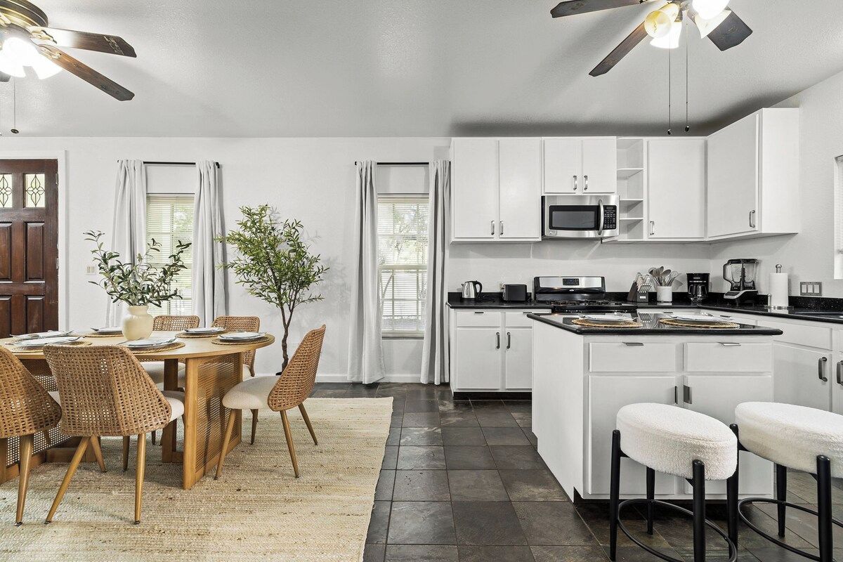A modern kitchen with white cabinets, a microwave, and a stove. There is a dining area with a table and chairs.