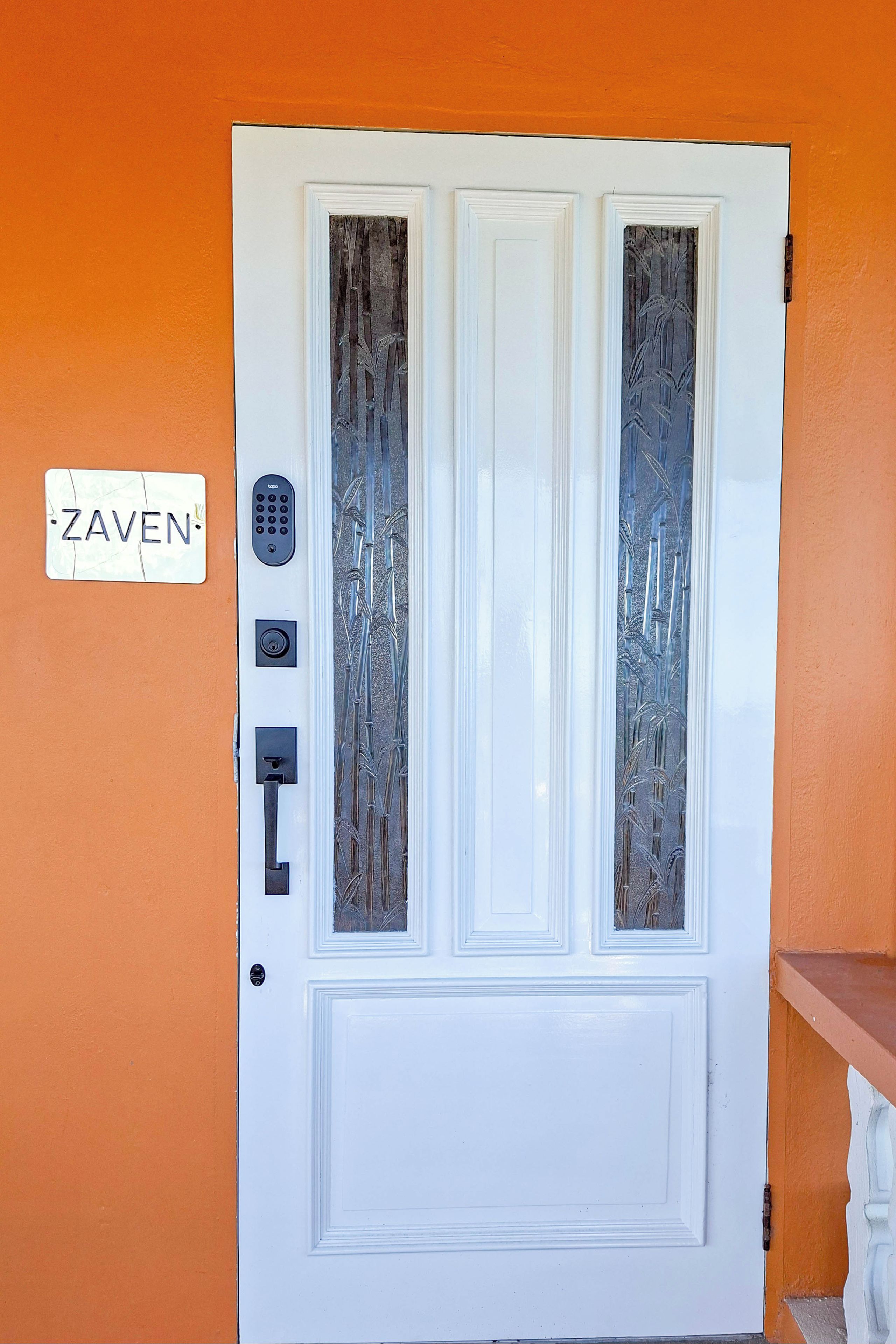Une porte blanche dotée d’un clavier et d’une plaque sur le mur portant l’inscription « ZAVEN ».