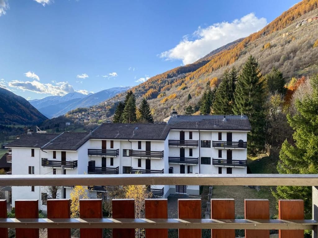 A row of white buildings with balconies, set against a mountainous backdrop.
