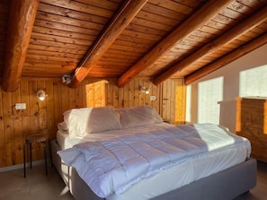 A bedroom with a wooden ceiling, a bed with white bedding, a nightstand, and a window with daylight. - AffittiPontediLegno - Panorama 3B (Temù)