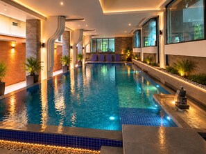 Una piscina interior con agua cristalina, rodeada de paredes con iluminación integrada y plantas en macetas.