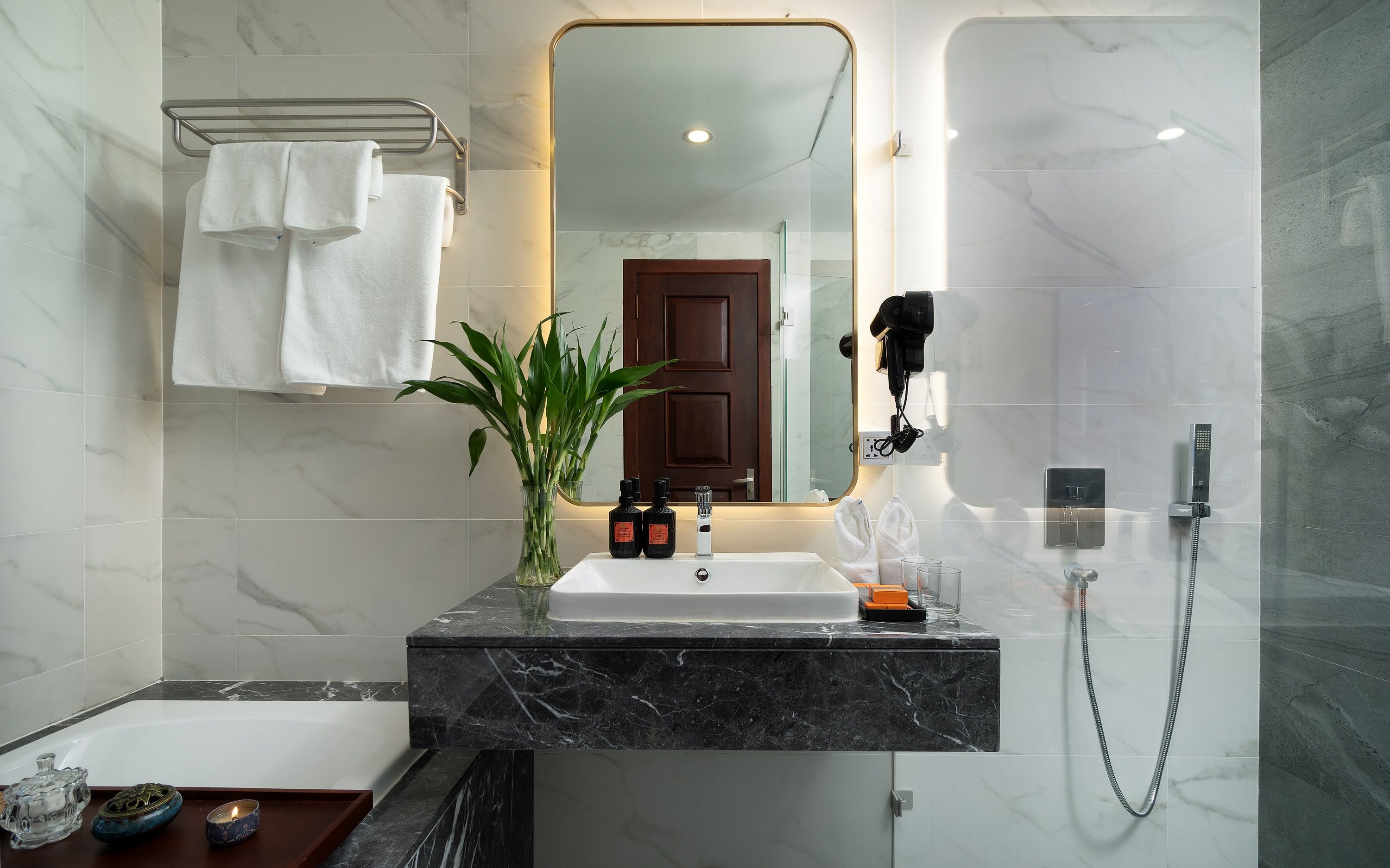 A modern bathroom with a marble sink, a handheld showerhead, and a large mirror.