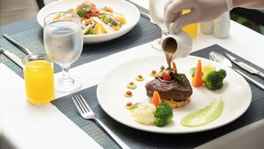 Ruokapöydällä on lautanen täynnä ruokaa, lasi vettä ja lasi mehua.