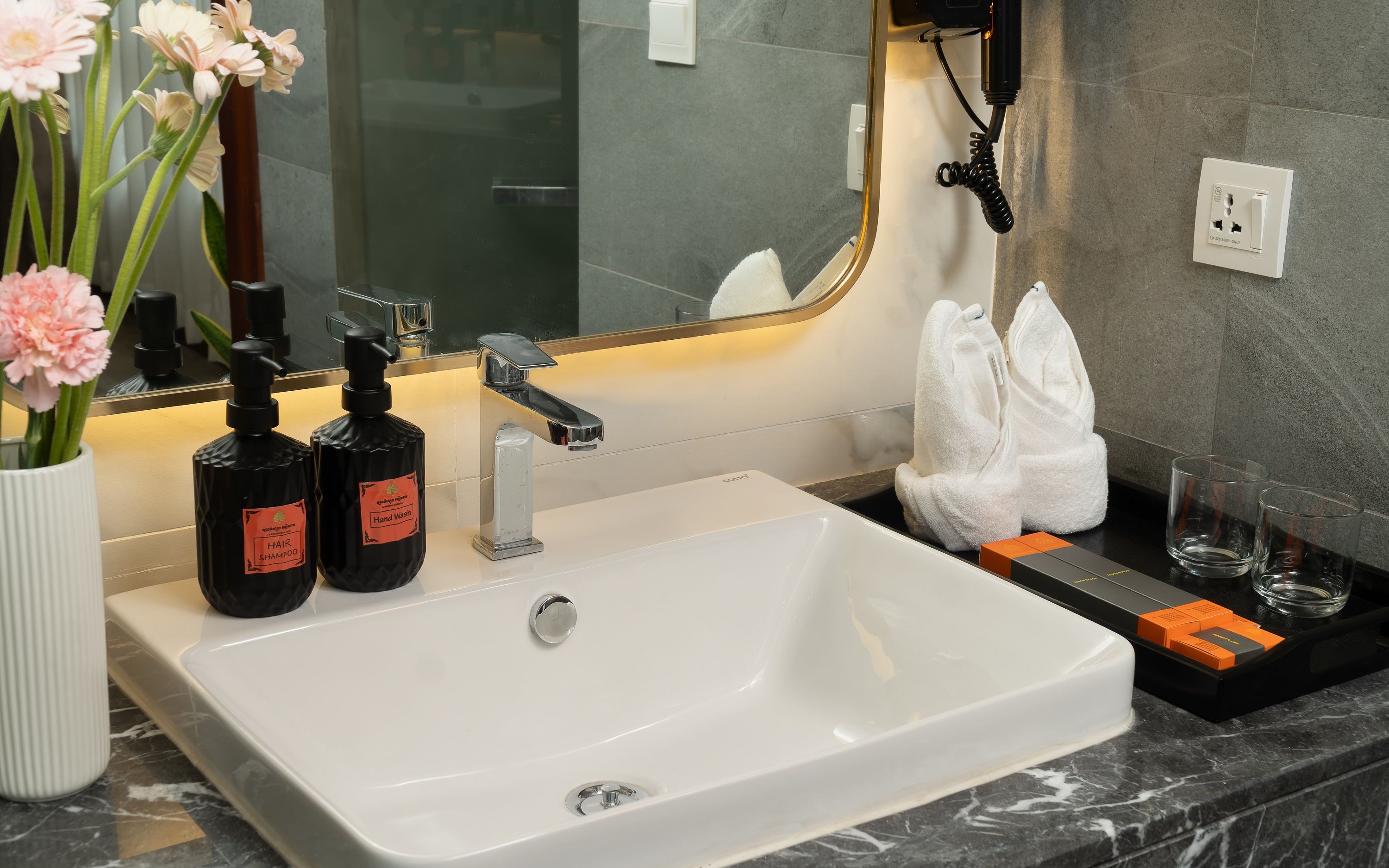 A hotel bathroom with a white sink, hand soap, shampoo, and a towel rack.