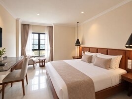 Habitación de hotel con una cama grande, un escritorio con silla, una mesita y un ventanal con cortinas.