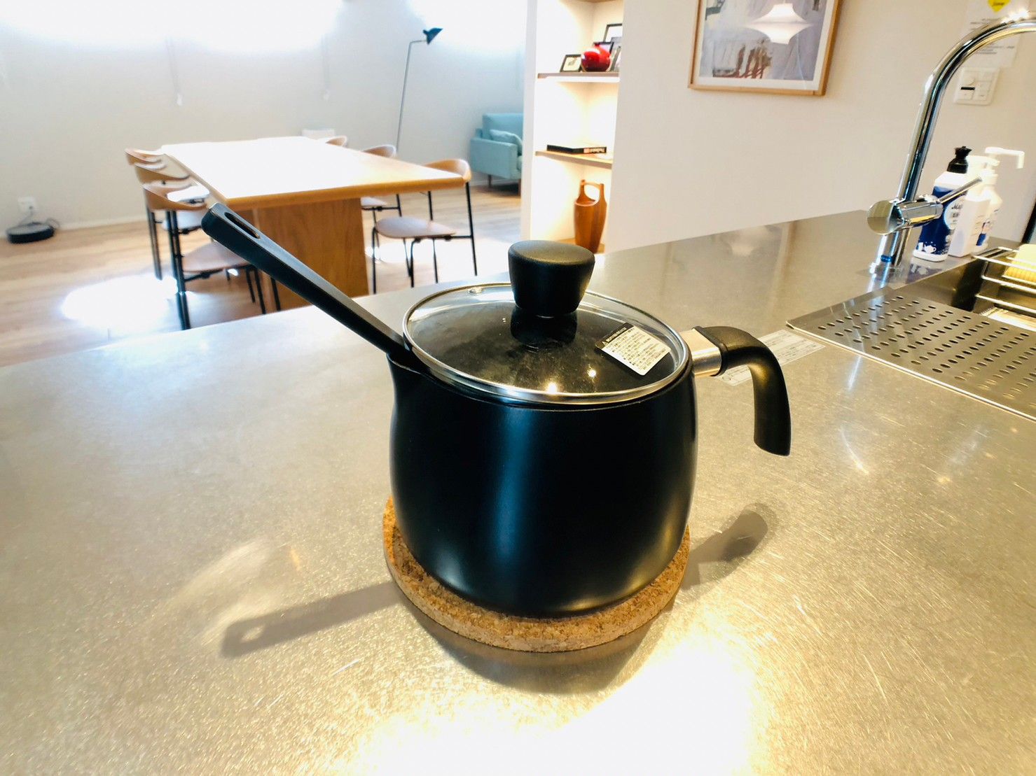 Una cocina con encimera de acero inoxidable, una olla negra con tapa y un posavasos de corcho.