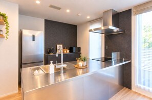 A modern kitchen with a stainless steel island, built-in appliances, and a large window providing natural light. - VILLA  Sasebo Stad SS1 (Sasebo)