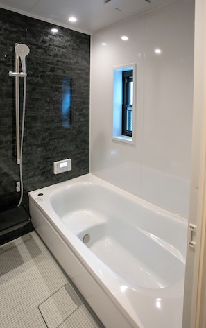 Un baño moderno con una bañera grande, zona de ducha con cabezal de ducha manual y un ventanal que proporciona luz natural.