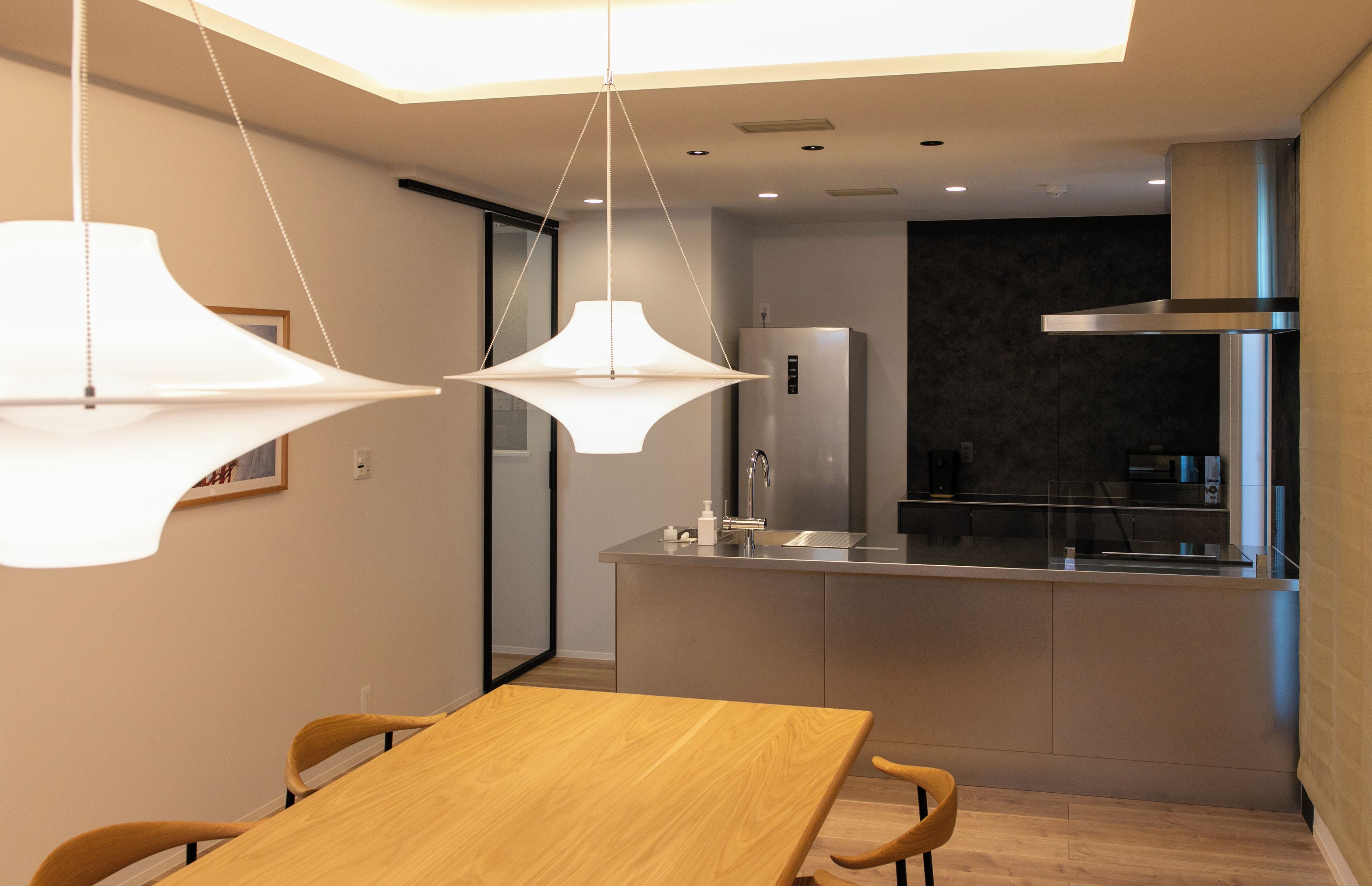 Una cocina moderna con una isla central, luces colgantes y un comedor con mesa y sillas de madera.