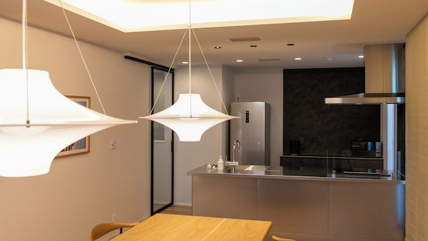Una cocina moderna con una isla central, luces colgantes y un comedor con mesa y sillas de madera.