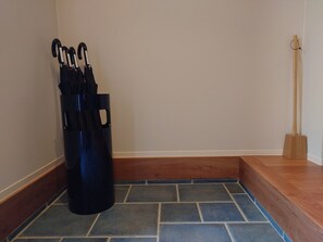 A corner of a room with a black trash bin, a wooden floor, and a wooden bench.