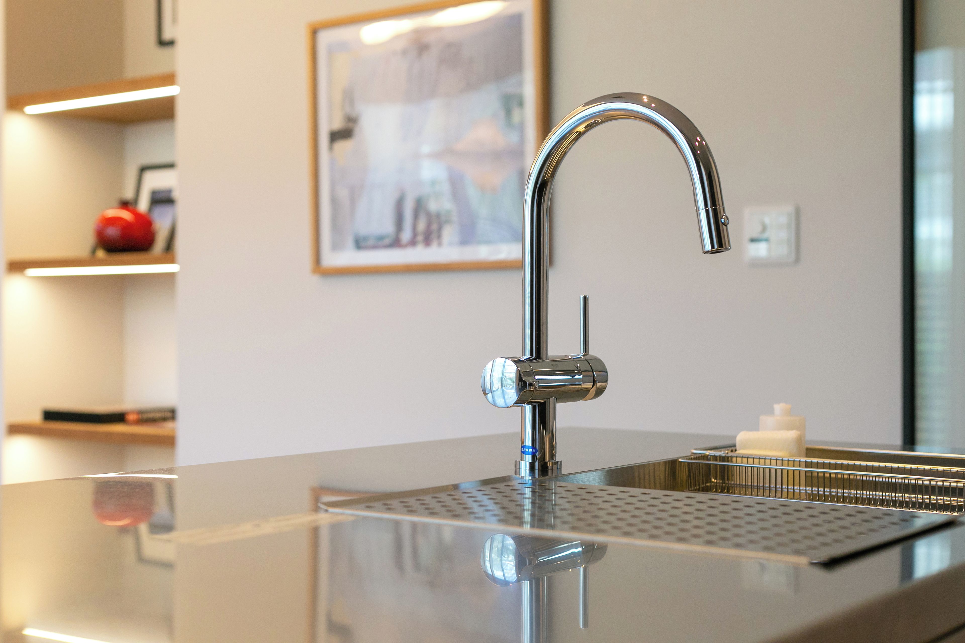 A modern kitchen with a stainless steel faucet, a reflective countertop, and a framed artwork on the wall.