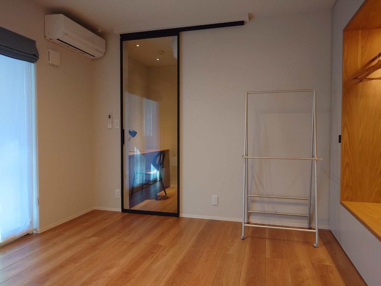 A room with a sliding glass door leading to a bathroom, a metal drying rack, and a wooden floor.