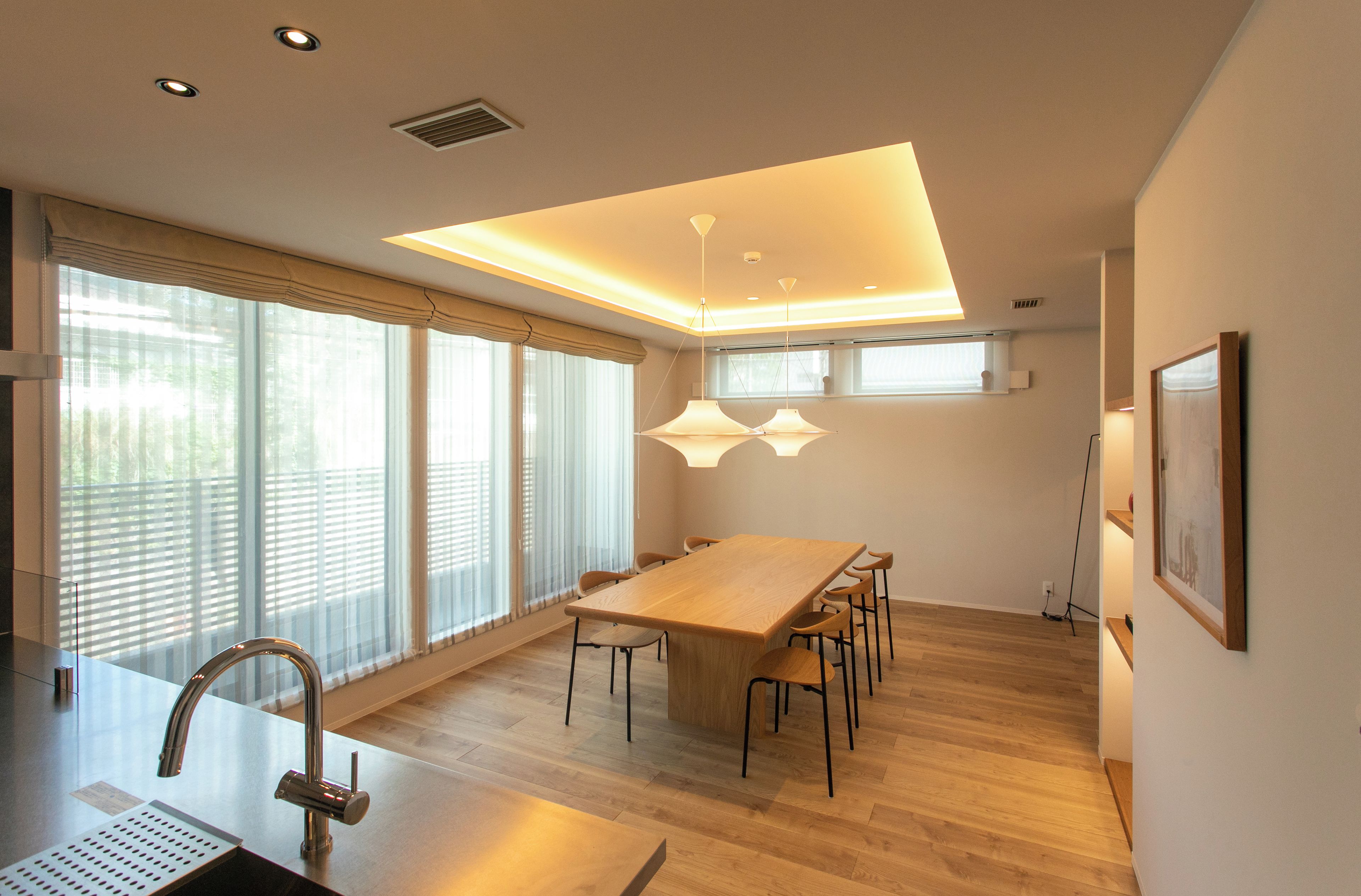 A modern kitchen with a wooden table and chairs, a stainless steel sink, and pendant lighting.