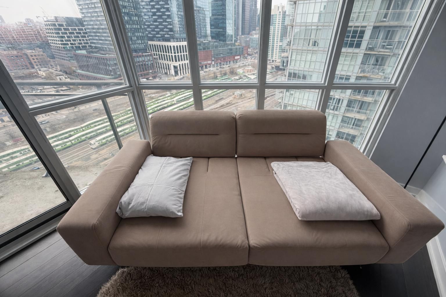 Een moderne bank met twee kussens in een kamer met grote ramen met uitzicht op een stadsbeeld.