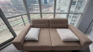 Een moderne bank met twee kussens in een kamer met grote ramen met uitzicht op een stadsbeeld.