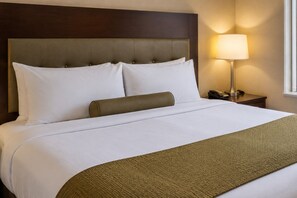 Una habitación de hotel con cama, cabecero, lámpara de noche y mesita.