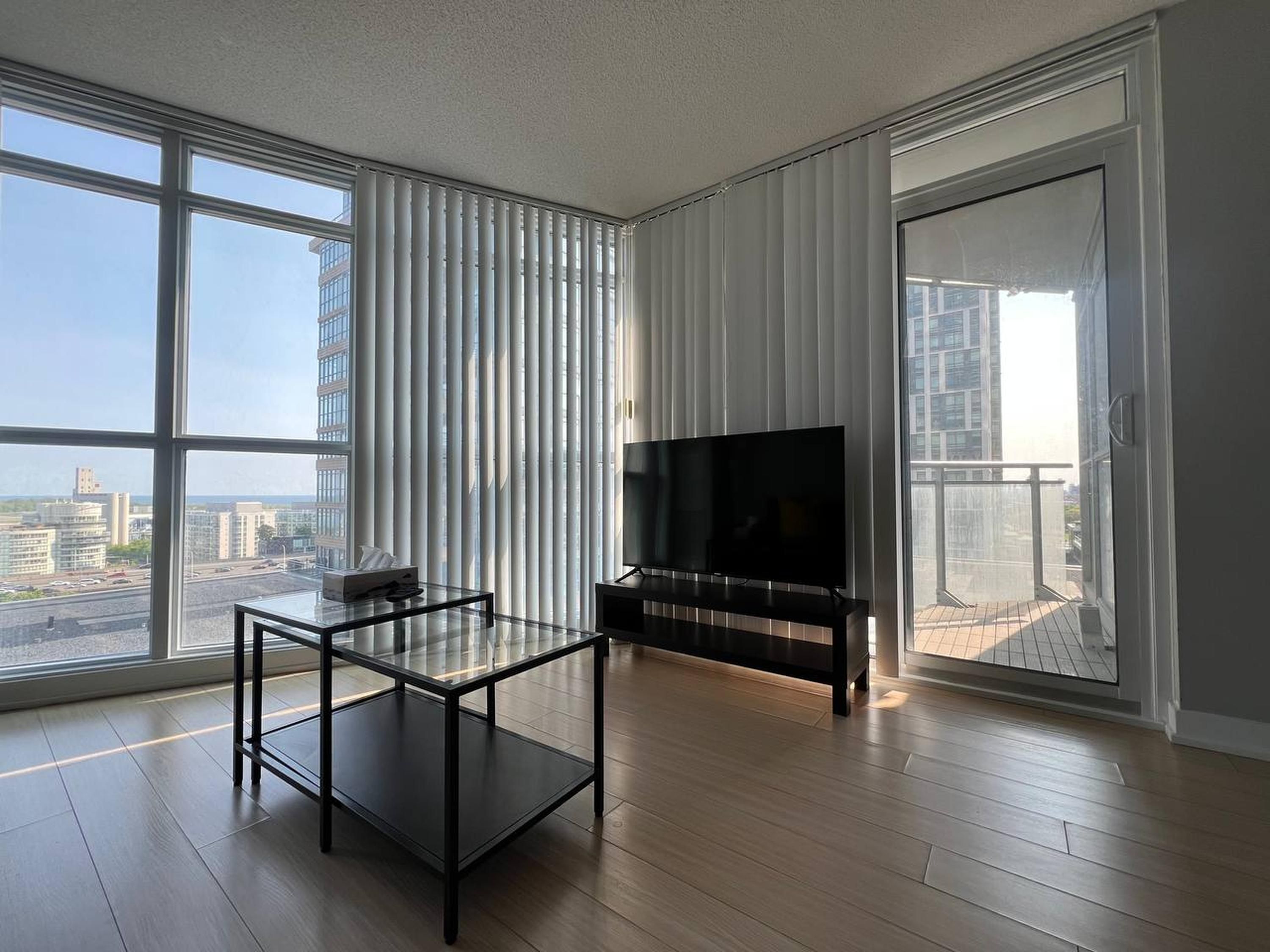 A modern living room with a large window, a flat-screen TV, and a glass coffee table.
