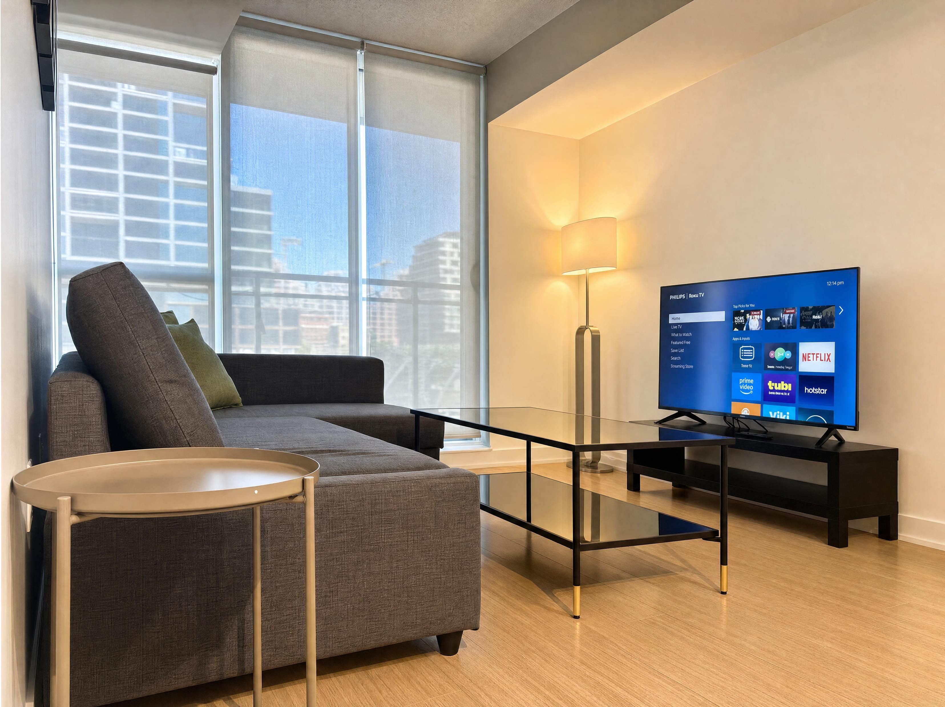 A modern living room with a sofa, a glass coffee table, a TV, and a lamp.