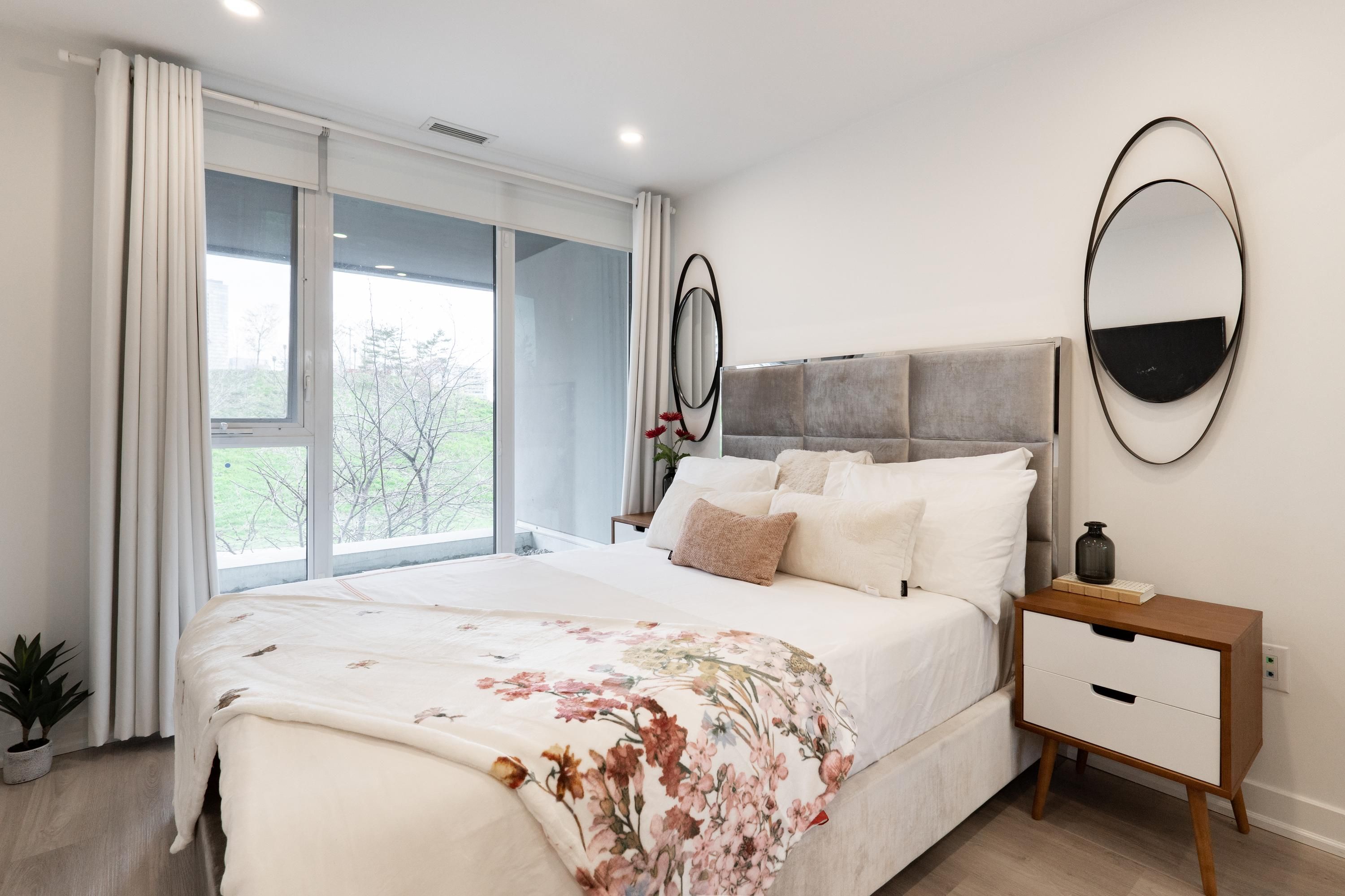 Een slaapkamer met een bed, nachtkastje en een groot raam.