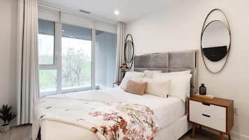 Een slaapkamer met een bed, nachtkastje en een groot raam.