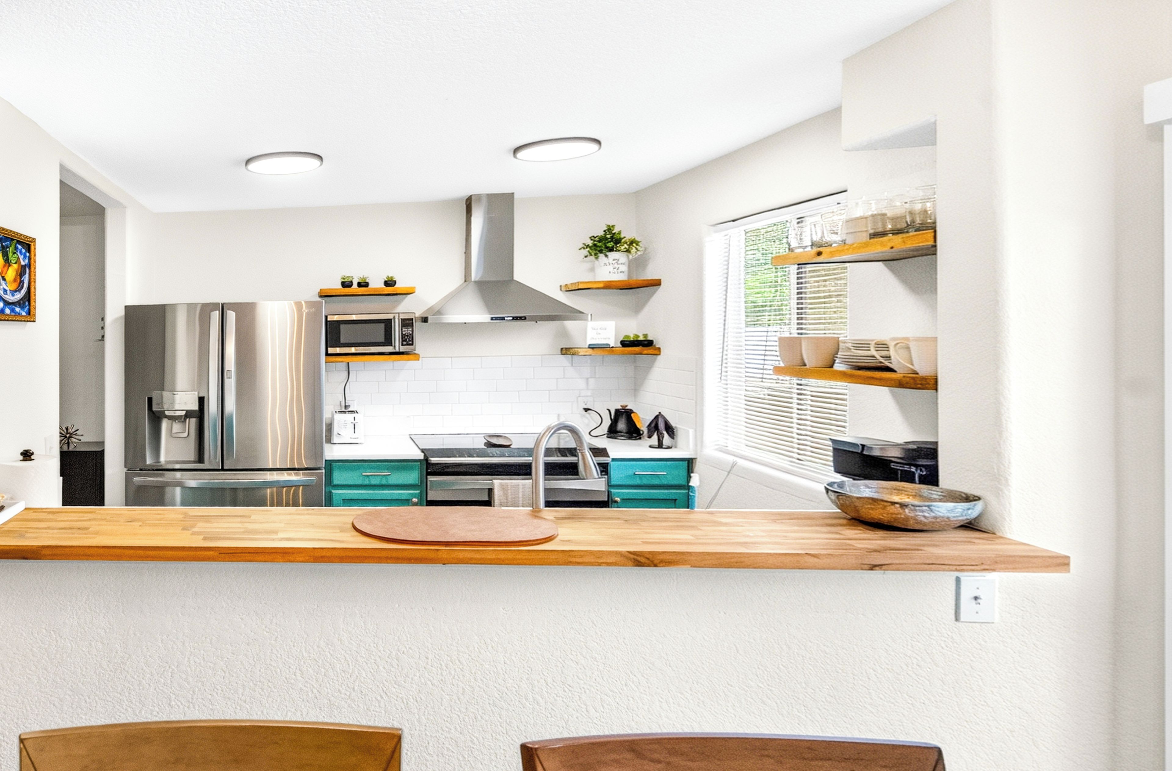A modern kitchen with a central island, stainless steel appliances, and a window with blinds.