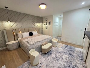 A modern bedroom with a bed, bedside tables, a nightstand, a headboard with integrated lighting, a rug, and a wall-mounted light fixture.