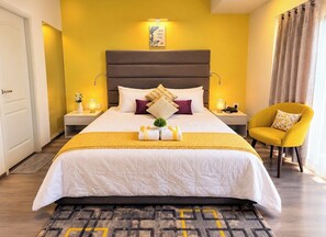 Ein Hotelzimmer mit einem großen Bett, einem Nachttisch mit Lampe, einem Sessel und Blick ins Freie.