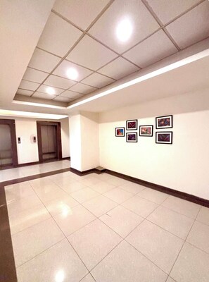 A hallway with a tiled floor, recessed lighting, and a wall with framed pictures. - Serene Luxe Studio - Pool & Gym (Gurugram)