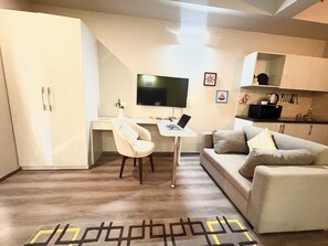 A compact living space with a kitchenette, a sofa, a desk with a laptop, and a TV. - Serene Luxe Studio - Pool & Gym (Gurugram)