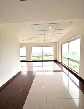 A spacious, empty room with large windows and a tiled floor. - Serene Luxe Studio - Pool & Gym (Gurugram)