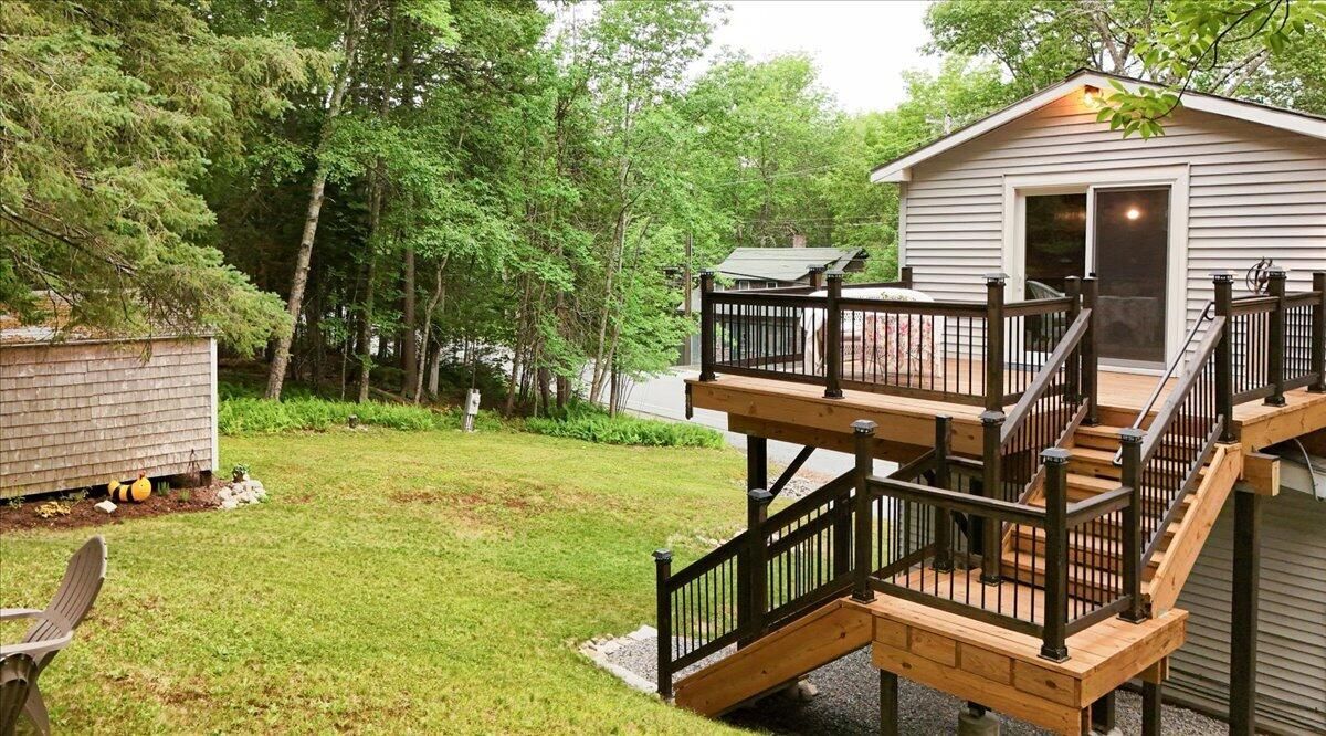 A two-story deck with a staircase leading to a covered entryway, surrounded by a grassy yard and trees.