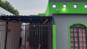 Edifício com fachada verde, entrada protegida por portão e área de varanda coberta.