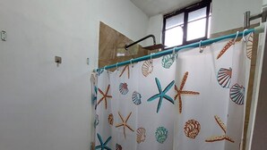 Casa de banho com sanita, cortina de chuveiro estampada com tema de estrela-do-mar e conchas, e janela sobre o chuveiro.