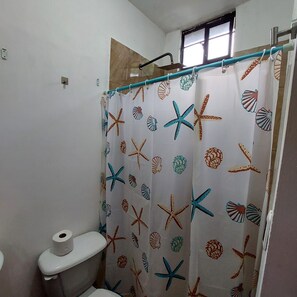 A bathroom with a toilet, a shower curtain with a starfish and shell pattern, and a window above the shower. - Casa Ju (Pet-Friendly) (Ciudad Valles)