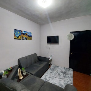 A living room with a grey sofa, a flat-screen TV mounted on the wall, and a black door. - Casa Ju (Pet-Friendly) (Ciudad Valles)