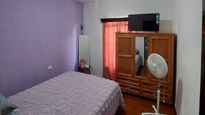 Quarto com cama, guarda-roupa, televisão, ventoinha e ar condicionado.