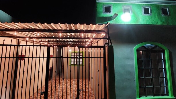 Uma área cercada com piso ladrilhado, portão de metal e um edifício com moldura de janela verde.