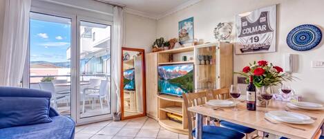 Un salon moderne comprenant un canapé, une table à manger et des chaises, un téléviseur, ainsi qu’un balcon offrant une vue panoramique.