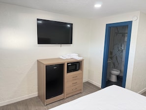 Habitació d'hotel amb llit, nevera minibar, televisió i zona de dutxa.