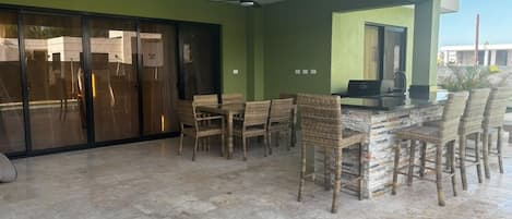 A covered outdoor seating area with wicker chairs and a bar counter.